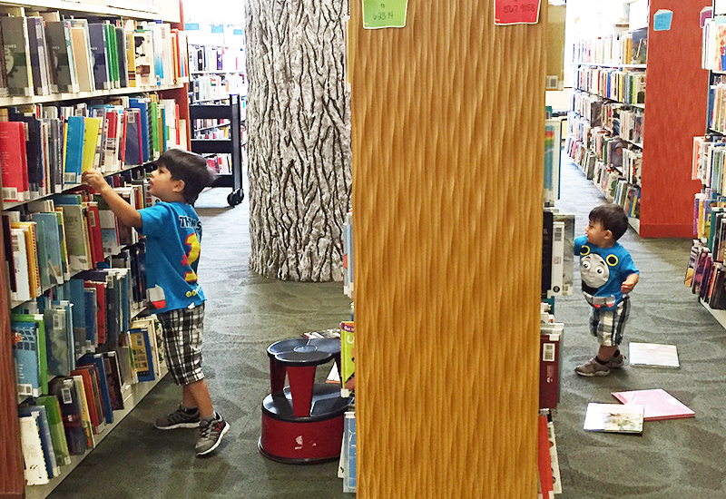 Two kids looking through book stacks in the Children's Room, 2016